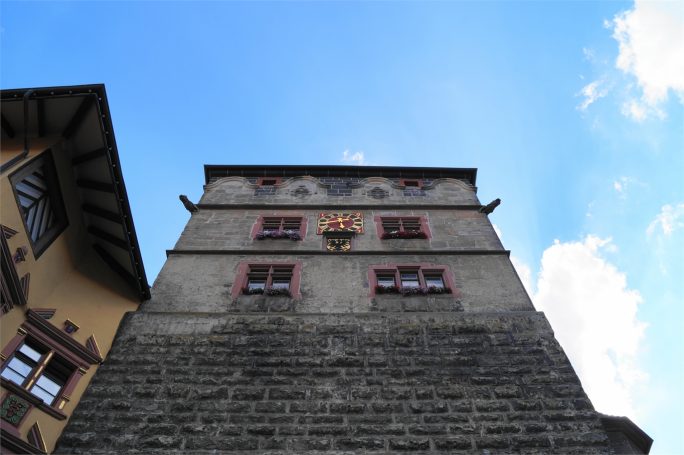 Blick nach oben auf ein historisches Gebäude mit bunten Fenstern und Wappen.